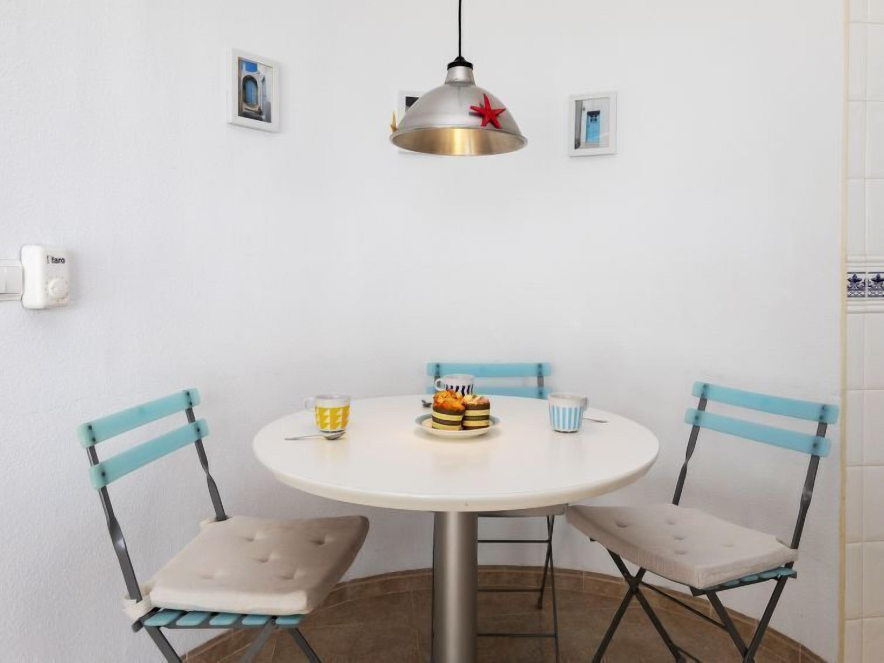 A round dining table with two chairs, a pendant light, and a small plate of pastries.
