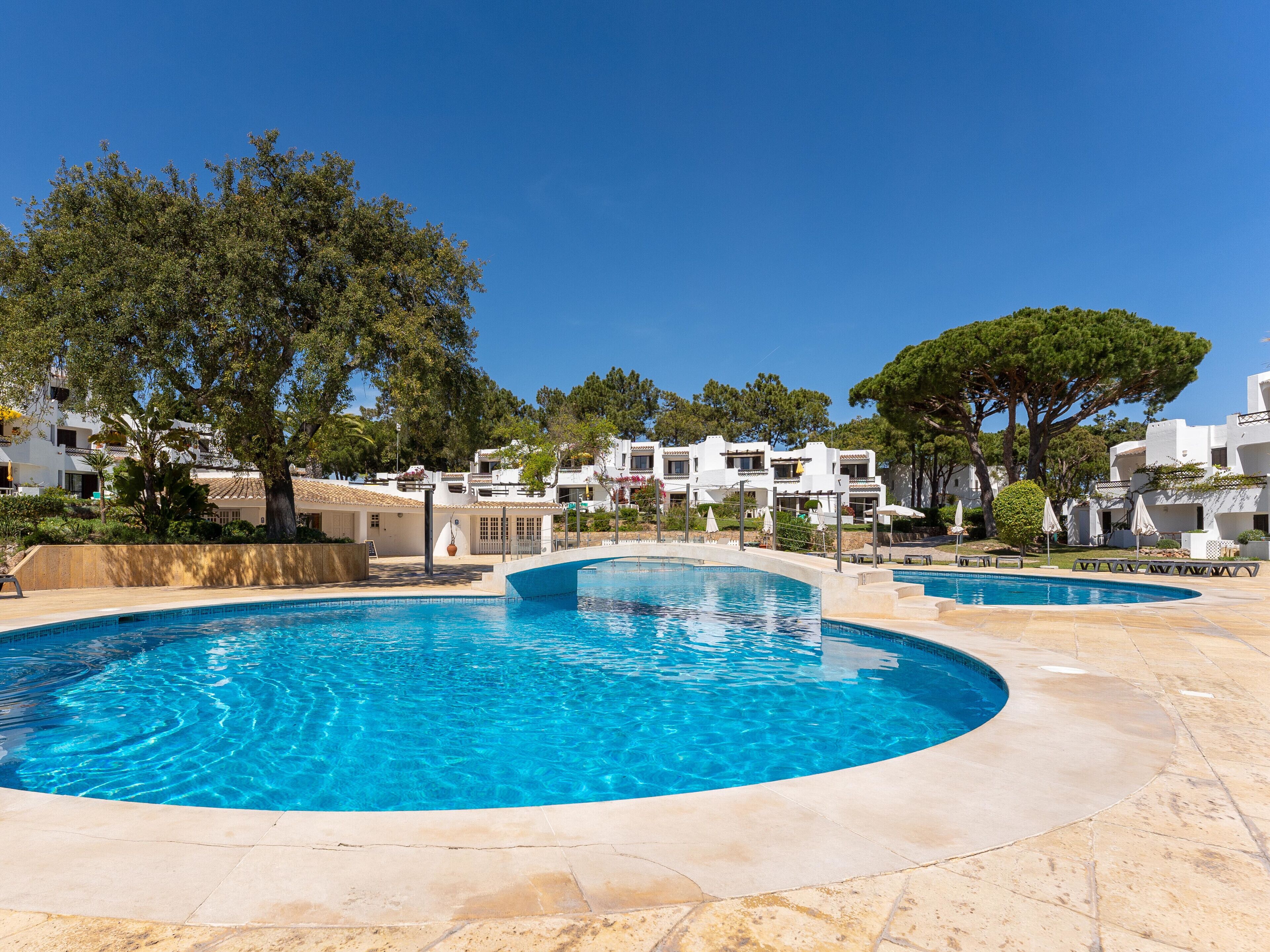 A swimming pool with a curved edge, surrounded by a paved area and white buildings with balconies.