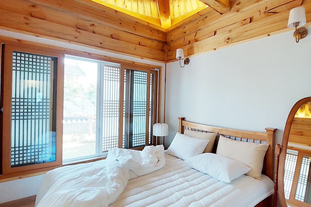 Une chambre dans une cabane en bois, avec un lit, une table de chevet, un miroir et des fenêtres à cadre en bois.