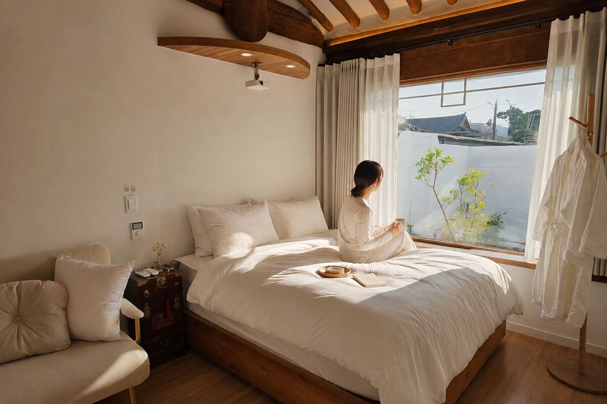 Une chambre à coucher comprenant un lit, une chaise, une table de chevet, une fenêtre avec des rideaux et une vue sur une étendue d’eau.