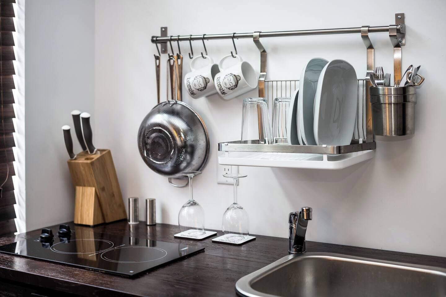 A kitchen with a stainless steel sink, a wooden knife block, a pot rack with hanging pots and a wine glass.