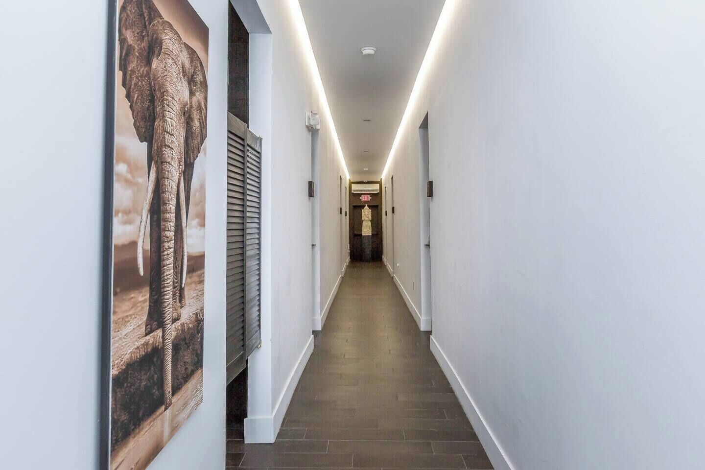 A hallway with a wooden floor, white walls, and a poster of an elephant.