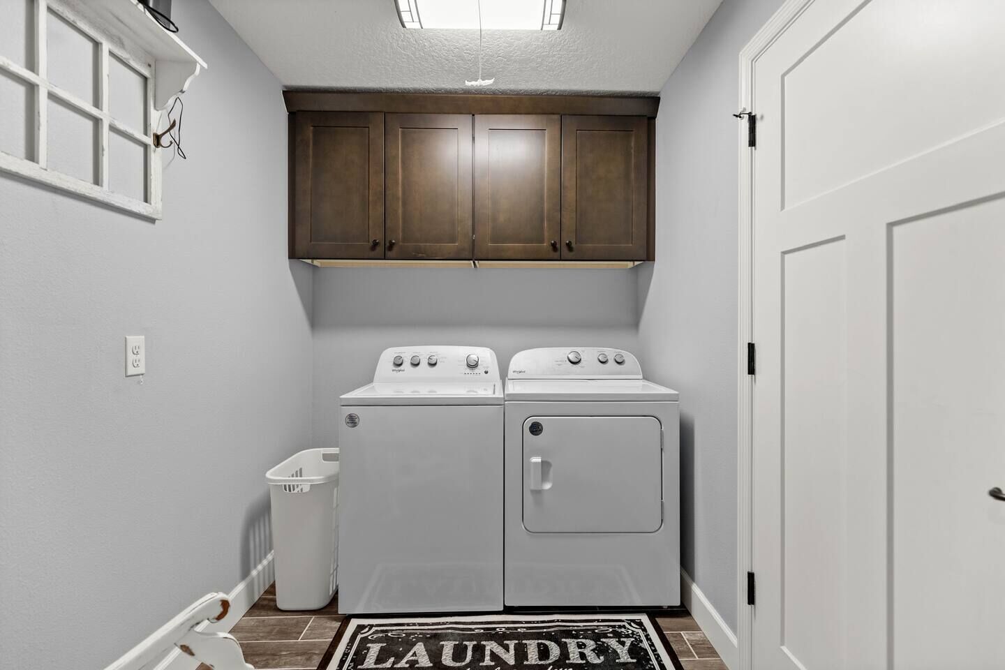 Un cuarto de lavado con dos lavadoras y secadoras apiladas, una cesta de ropa blanca y una alfombra con la palabra 'LAUNDRY'.