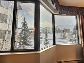 Une fenêtre d’angle donnant sur un paysage enneigé, avec des arbres et des bâtiments.