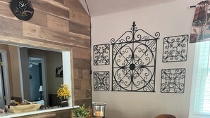 Ein Essbereich mit einem runden Holztisch, vier Holzsesseln mit gepolsterten Sitzen und einer Wand mit dekorativer Metallkunst.