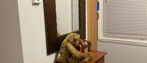 A wooden dresser with a mirror, a teddy bear, and a window with blinds.