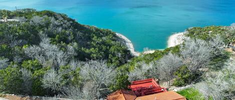 A coastal property with a red-roofed building, surrounded by dense greenery and overlooking a turquoise sea.