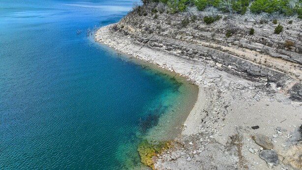 Un paisaje costero con aguas azules cristalinas, acantilados rocosos y vegetación escasa.