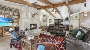 Un salón espacioso con chimenea de piedra, sofás de cuero, una mesa de centro de madera y una estantería llena de libros y objetos decorativos.