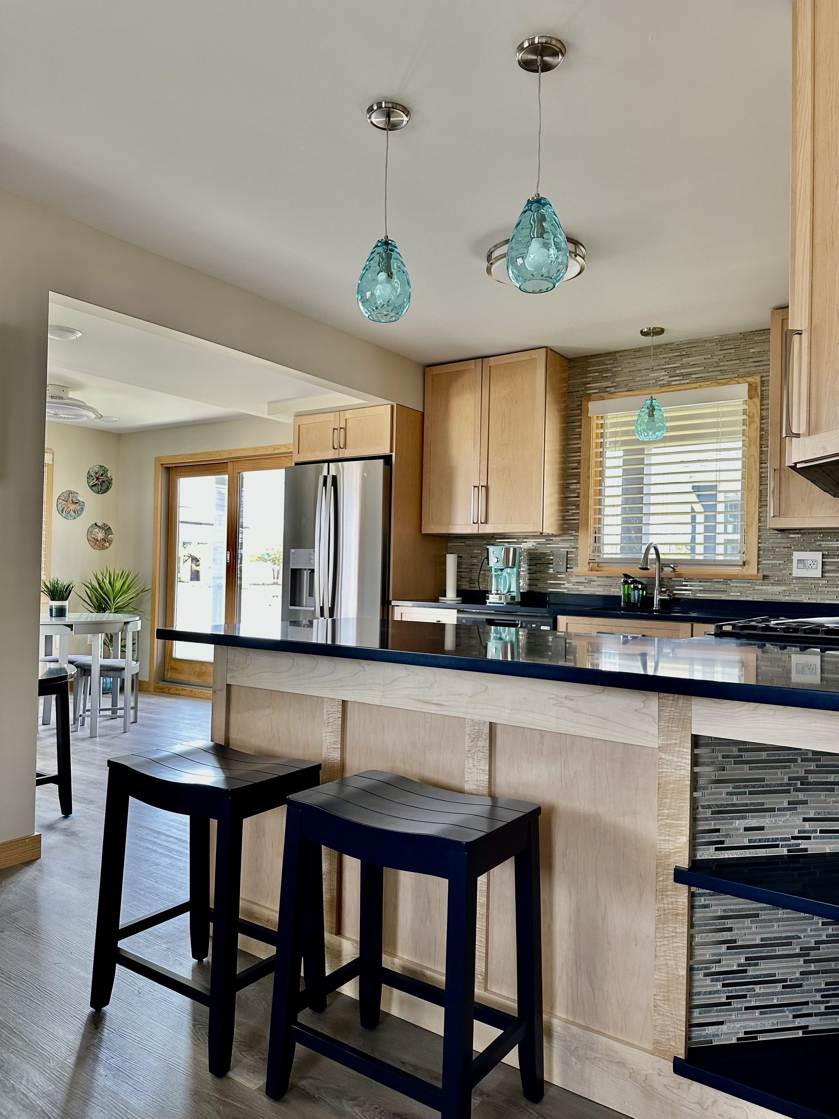 A modern kitchen with wooden cabinets, a stainless steel refrigerator, a built-in stove, and a large island with bar stools.