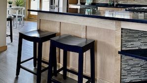 Eine moderne Küche mit Holzschränken, einem Edelstahl-Kühlschrank, einem eingebauten Herd und einer großen Kochinsel mit Barhocker.