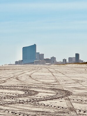 Une vaste étendue de sable à ciel ouvert, sillonnée de traces de pneus qui mènent vers les contours d’une ville.