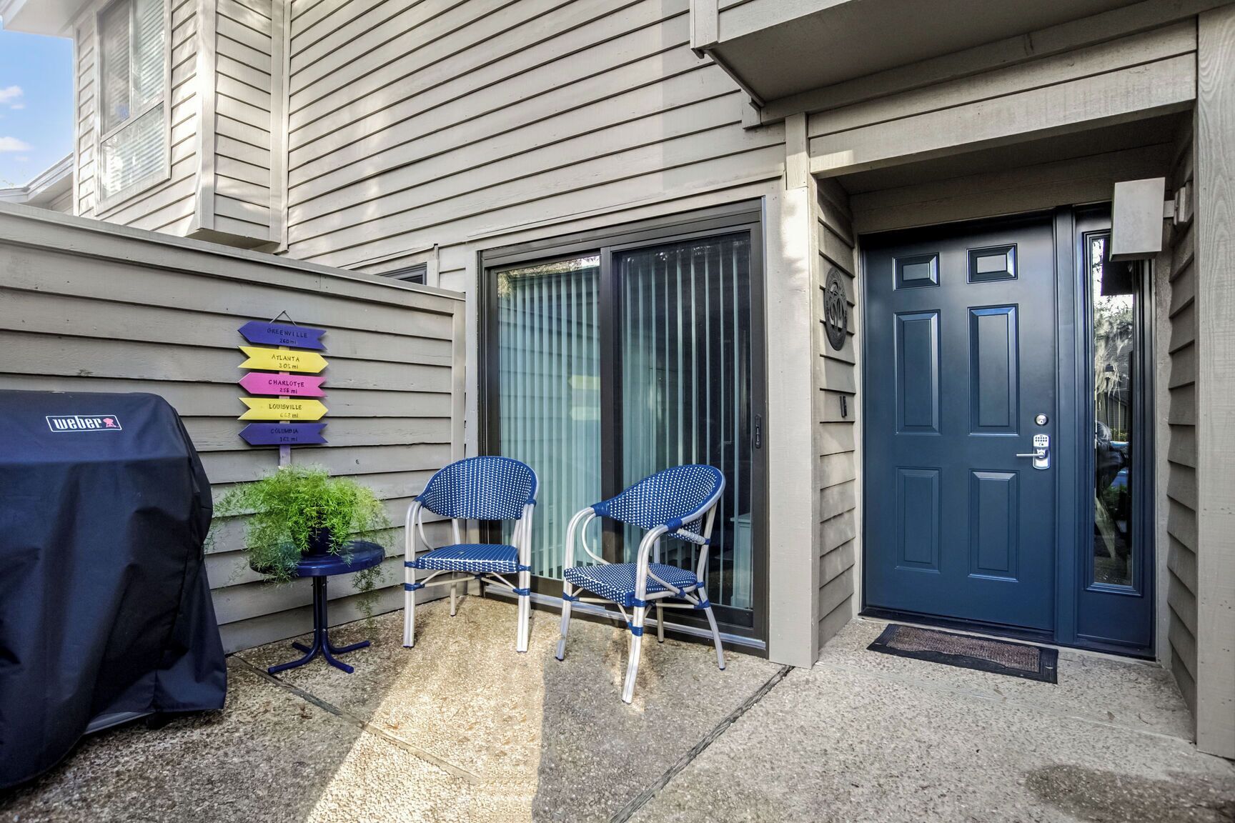 A patio with two chairs and a grill, a door, and directional signs on the wall.
