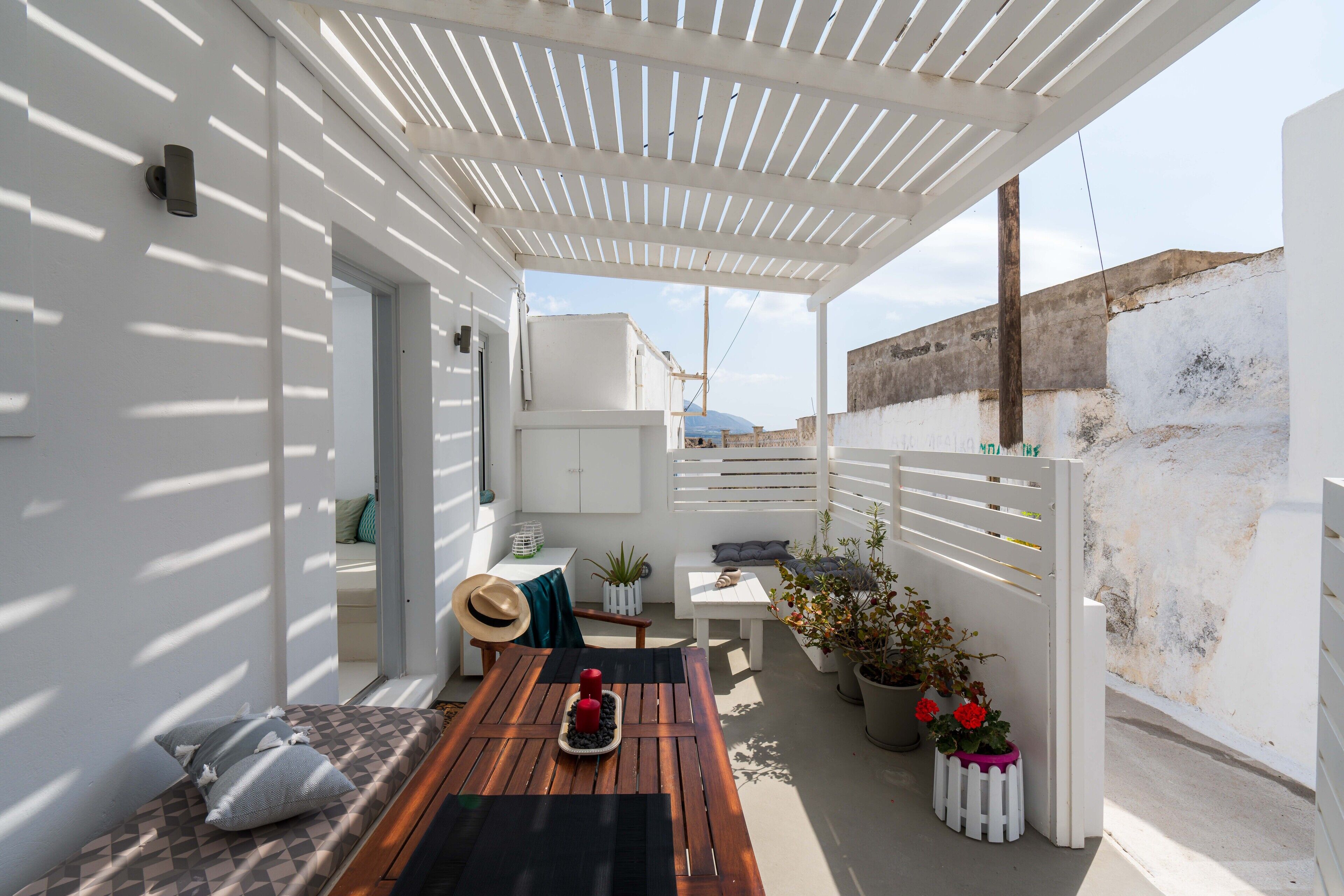 Un espacio al aire libre techado con una mesa de madera, cojines y plantas en macetas.