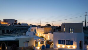 A coastal village with white-washed buildings, a small café with outdoor seating, and a clear view of the sea. - Santorita Suites (Santorini)