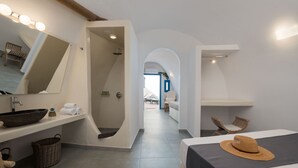 A modern hotel room with a large bed, a bathroom with a bathtub, and a view of the beach. - Santorita Suites (Santorini)