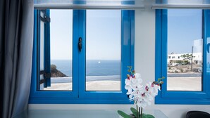 A room with a large window offering a view of the sea and a small boat. - Santorita Suites (Santorini)