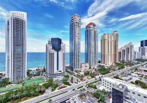 A high-rise urban area with multiple skyscrapers, a clear blue sky, and a view of the ocean.