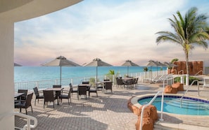 An outdoor pool area with lounge chairs and umbrellas, overlooking a body of water.