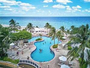 A resort pool area with a curved pool, lounge chairs, and palm trees.