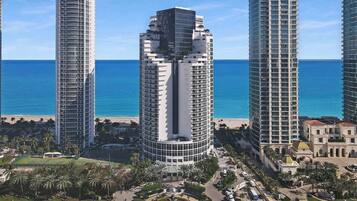 A high-rise hotel with a curved facade, located near a beach with palm trees and a clear blue sky.