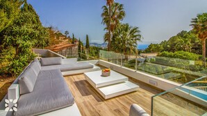 A modern outdoor living area with a sofa, a table, and a glass railing overlooking a scenic landscape.