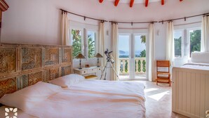 A bedroom with a large bed, a desk with a telescope, and a balcony with a view of the sea.