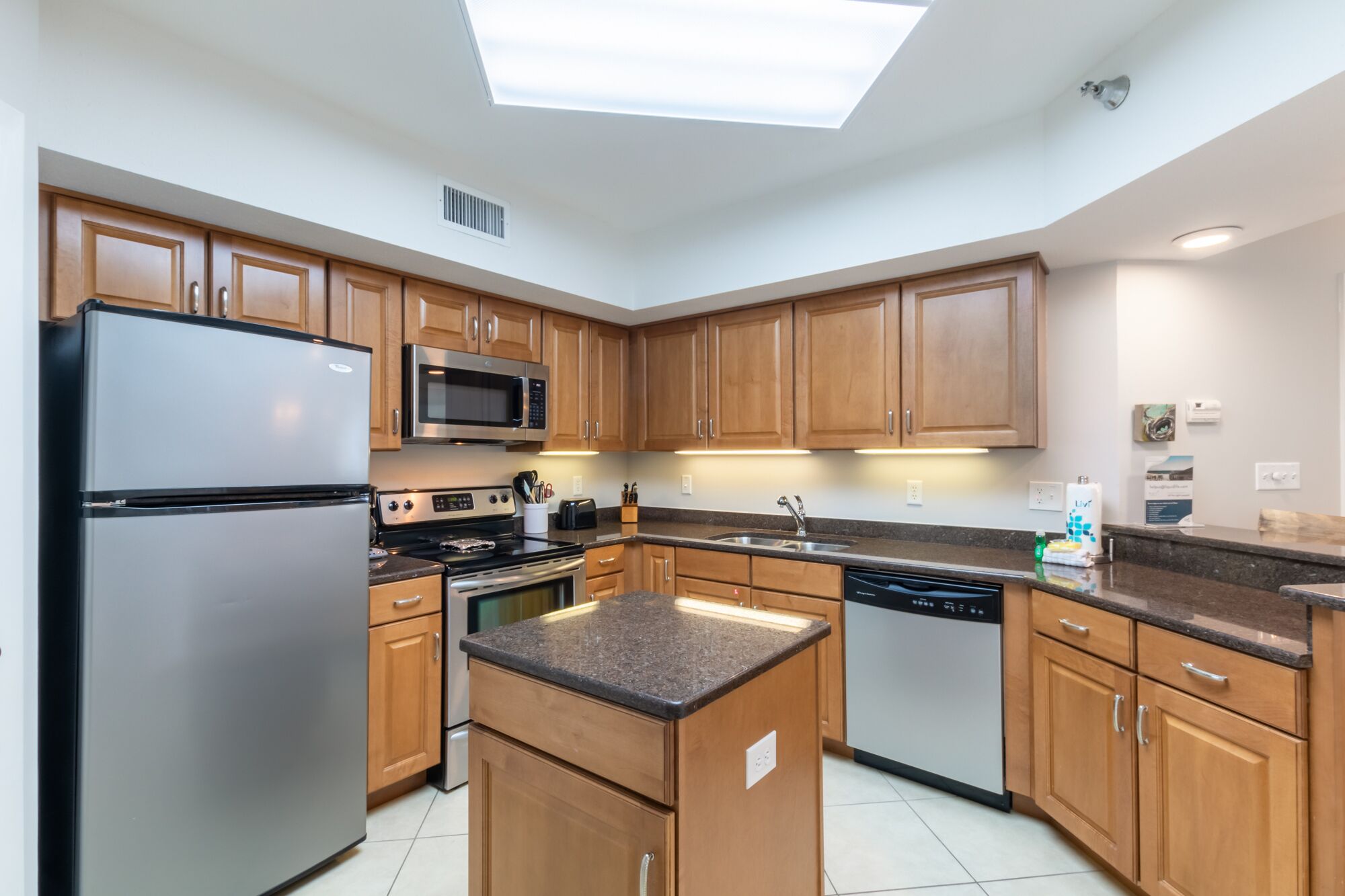 A modern kitchen with wooden cabinets, stainless steel appliances, and a skylight.