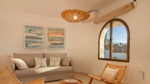 Ein gemütliches Wohnzimmer mit einer Couch, zwei Korbstühlen, einem kleinen runden Tisch und zwei abstrakten Bildern an der Wand.