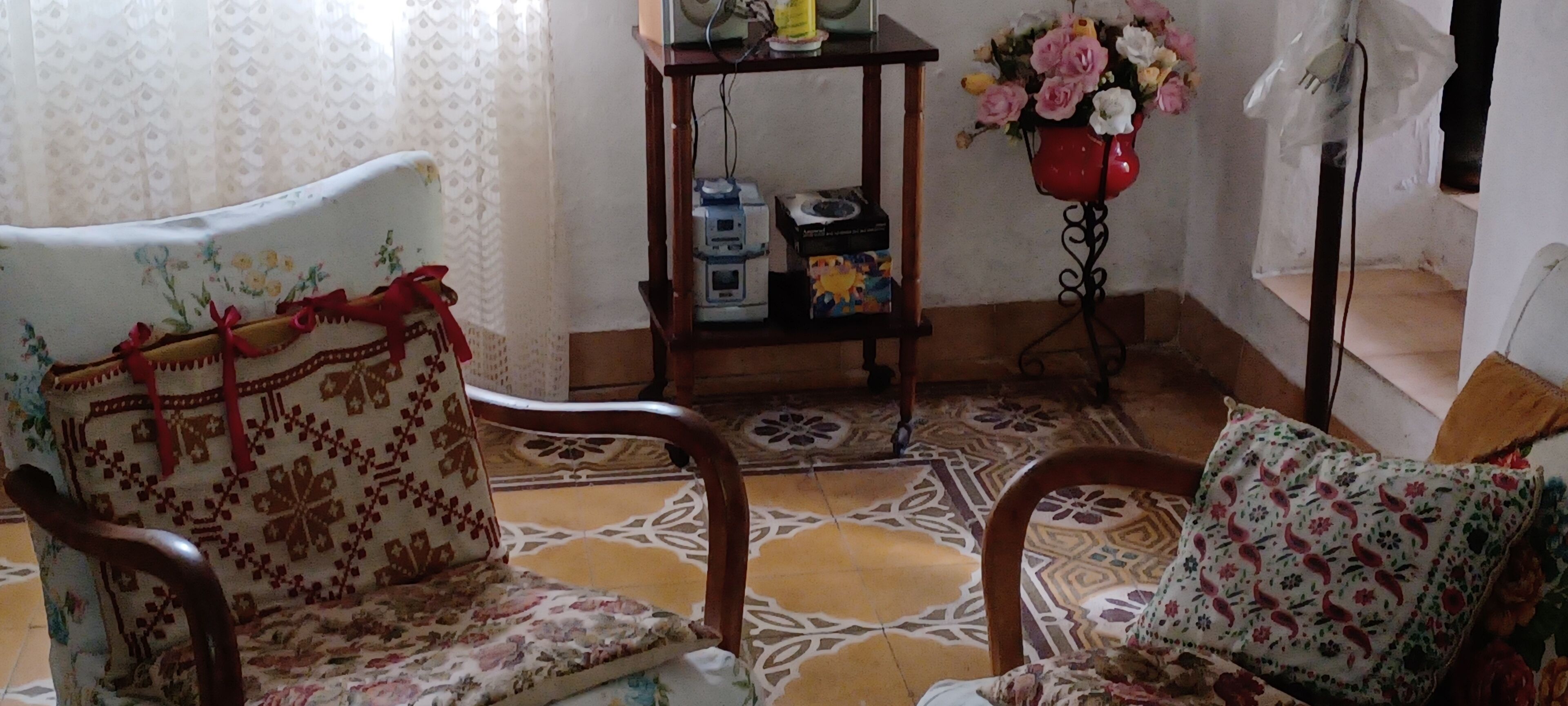 A room with patterned chairs, a small table with a vase of flowers, and a shelf with various items.