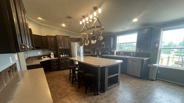 A modern kitchen with dark cabinetry, a central island with stools, a large window, and a hanging light fixture. - New Property at PK lake! (Graham)