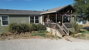 A two-story house with a porch, a covered outdoor seating area, and a small staircase leading to the entrance. - New Property at PK lake! (Graham)