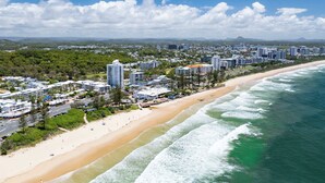 A coastal cityscape with beachfront hotels, a sandy beach, and ocean waves.