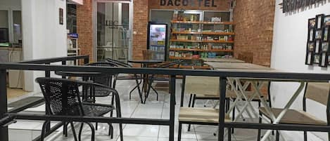 A cafe area with tables and chairs, a refrigerator, and shelves stocked with products.