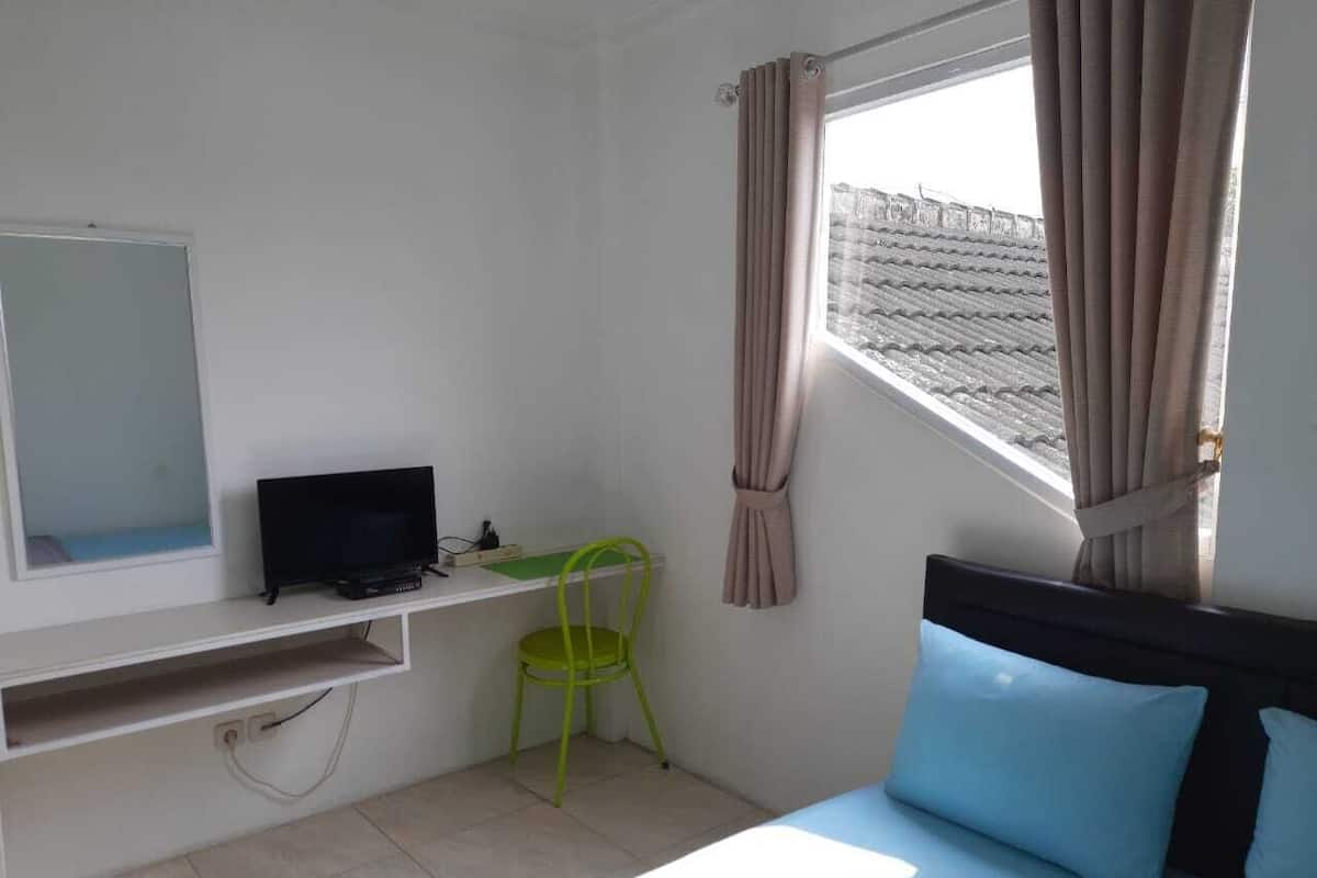 Un dormitorio con una cama, un escritorio con computadora, una silla y un ventanal con cortinas.
