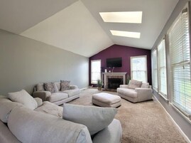 Una sala de estar con techo alto, chimenea y ventanas amplias.