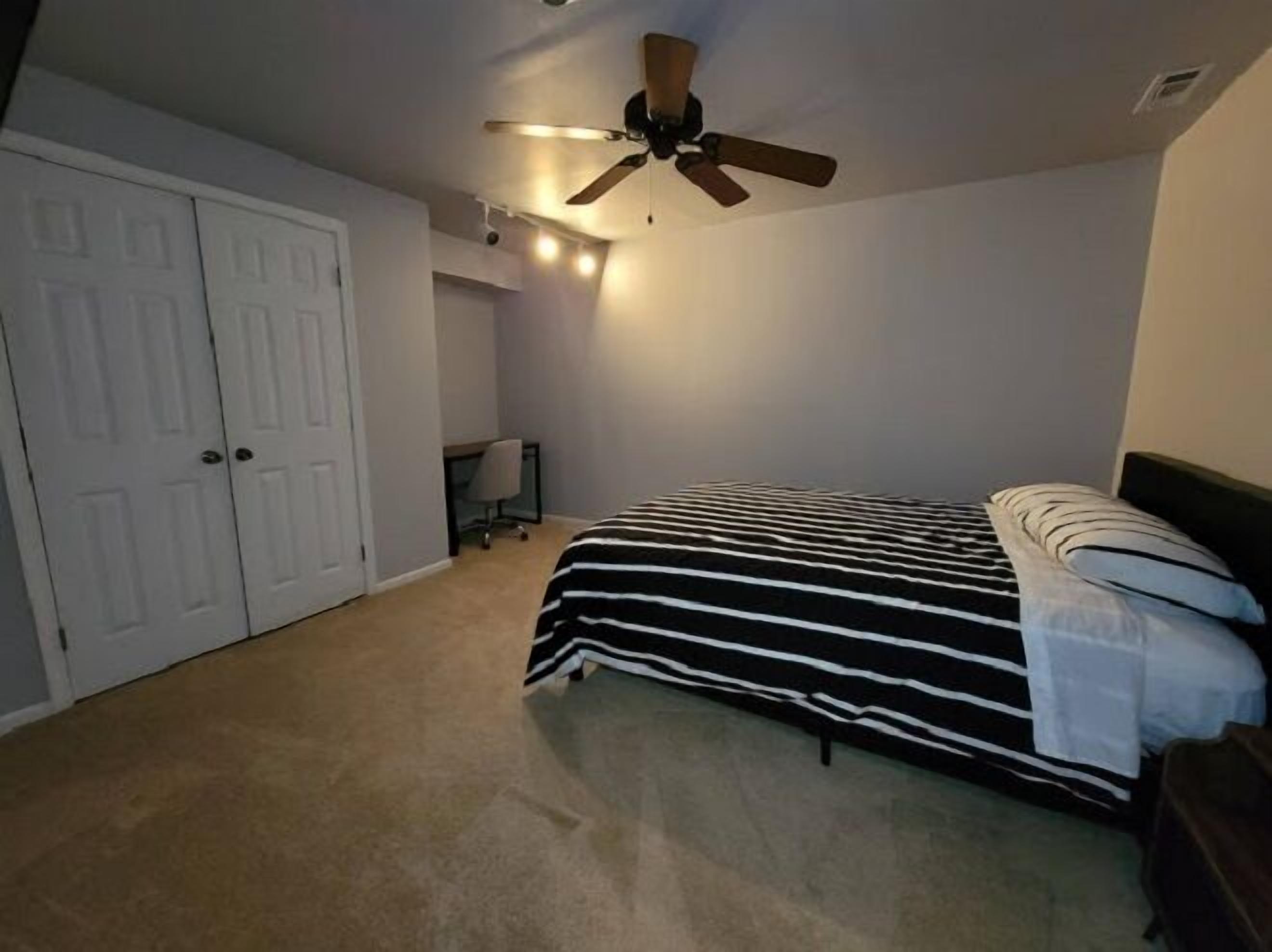 Une chambre à coucher avec un lit, un ventilateur de plafond et un bureau avec une chaise.