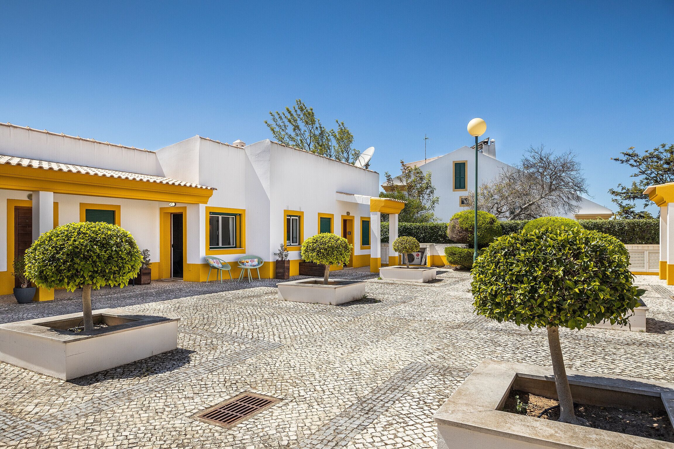 A courtyard with white buildings, yellow trim, and potted trees.