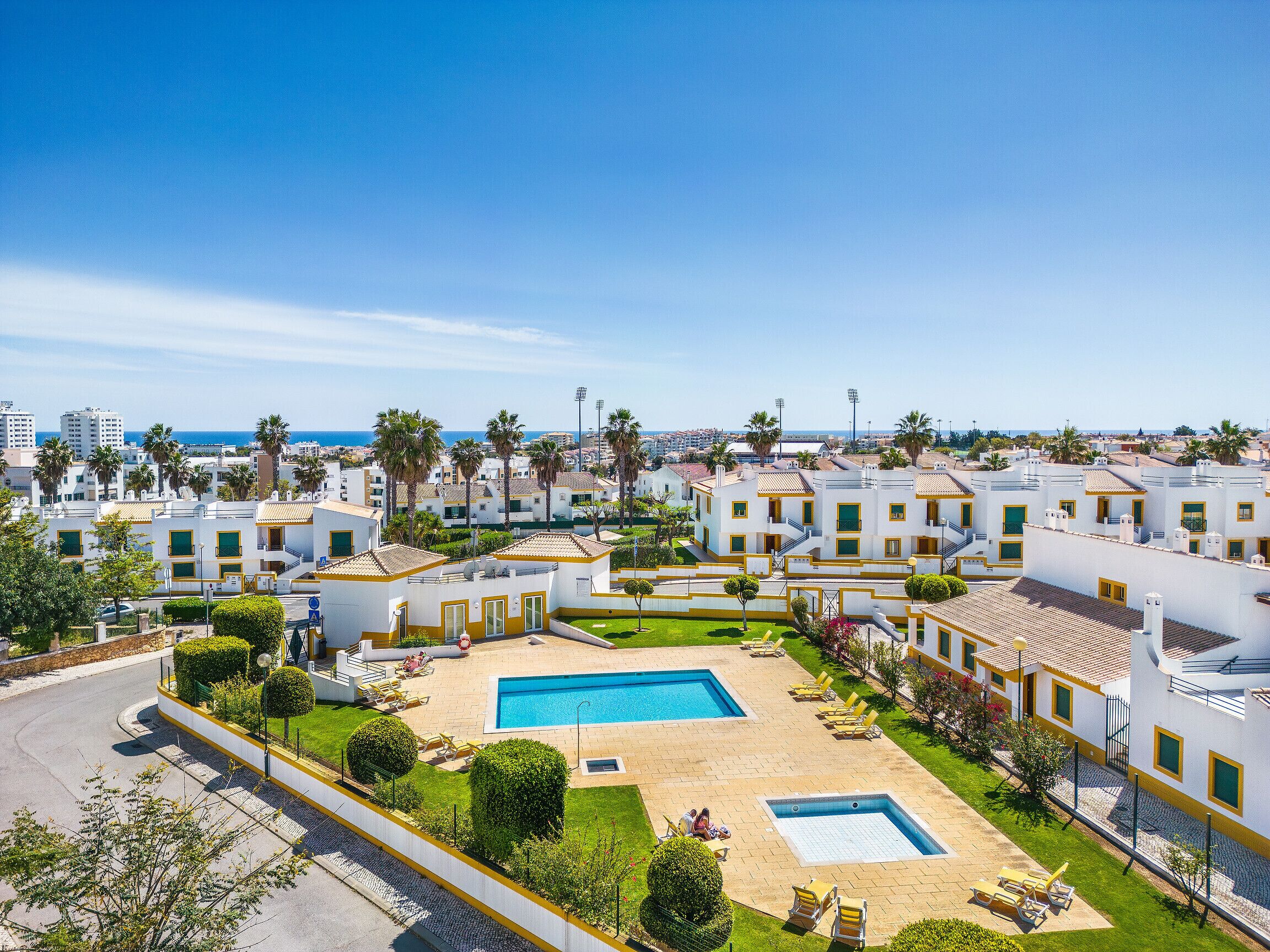 Een resort met meerdere witte gebouwen, een centraal gelegen zwembad en uitzicht op zee.