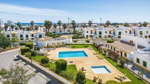Um resort com vários edifícios brancos, uma piscina central e vista para o mar.
