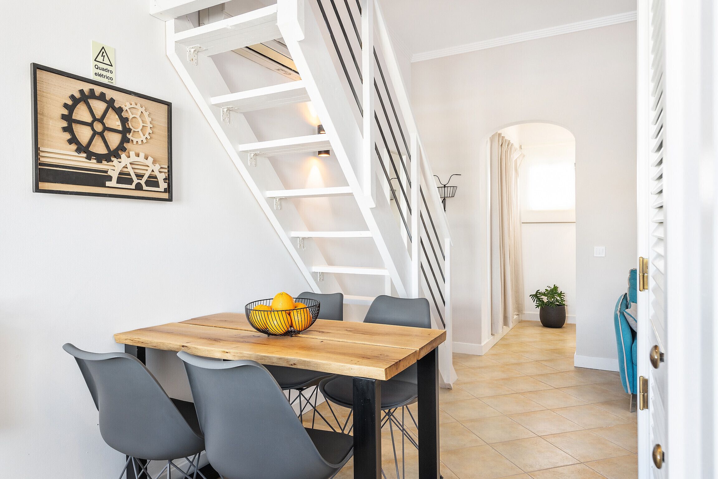 Een eethoek met een houten tafel en stoelen, een trap en een kunstwerk aan de muur.