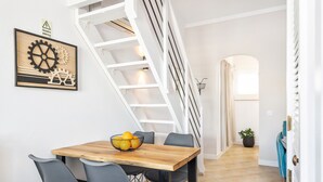 Uma área de refeições com uma mesa e cadeiras de madeira, uma escada e uma obra de arte na parede.