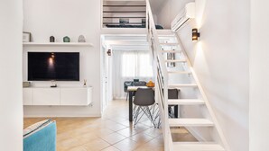 Um espaço de estar moderno com televisão na parede, escada com prateleiras embutidas e área de jantar com mesa e cadeiras.