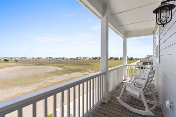 A covered porch with a view of a beach and houses in the distance.