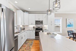 A modern kitchen with white cabinets, stainless steel appliances, a large island, and a wooden floor. - Fore Seasuns / 139 Scotch Bonnet Dr. 4 Bedroom Home by RedAwning (Supply)