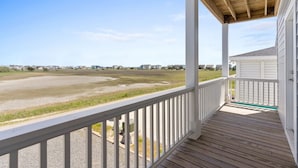 A covered porch with a view of a beach and houses in the distance. - Fore Seasuns / 139 Scotch Bonnet Dr. 4 Bedroom Home by RedAwning (Supply)