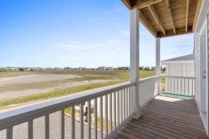 A covered porch with a view of a beach and houses in the distance. - Fore Seasuns / 139 Scotch Bonnet Dr. 4 Bedroom Home by RedAwning (Supply)