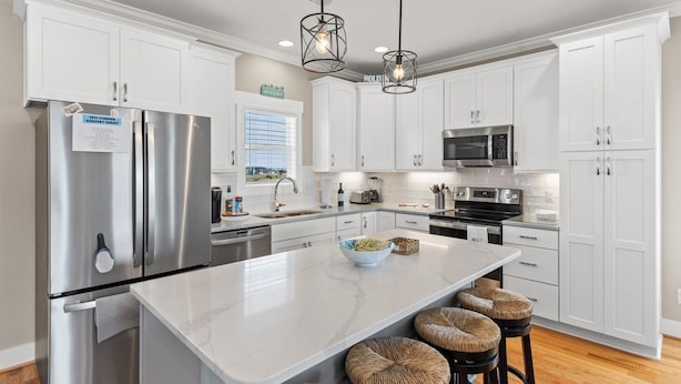 A modern kitchen with white cabinetry, stainless steel appliances, and a marble island with bar stools. - Fore Seasuns / 139 Scotch Bonnet Dr. 4 Bedroom Home by RedAwning (Supply)
