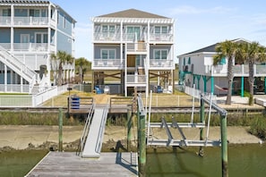 Une propriété située en bord de mer, comprenant un bâtiment à deux étages, une terrasse en bois et un petit quai pour bateaux.