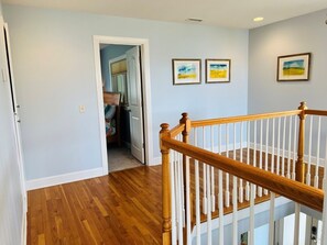 A hallway with wooden flooring, a white railing, and two framed pictures on the wall. - Fairway To Heaven 3 Bedroom Home by RedAwning (Supply)